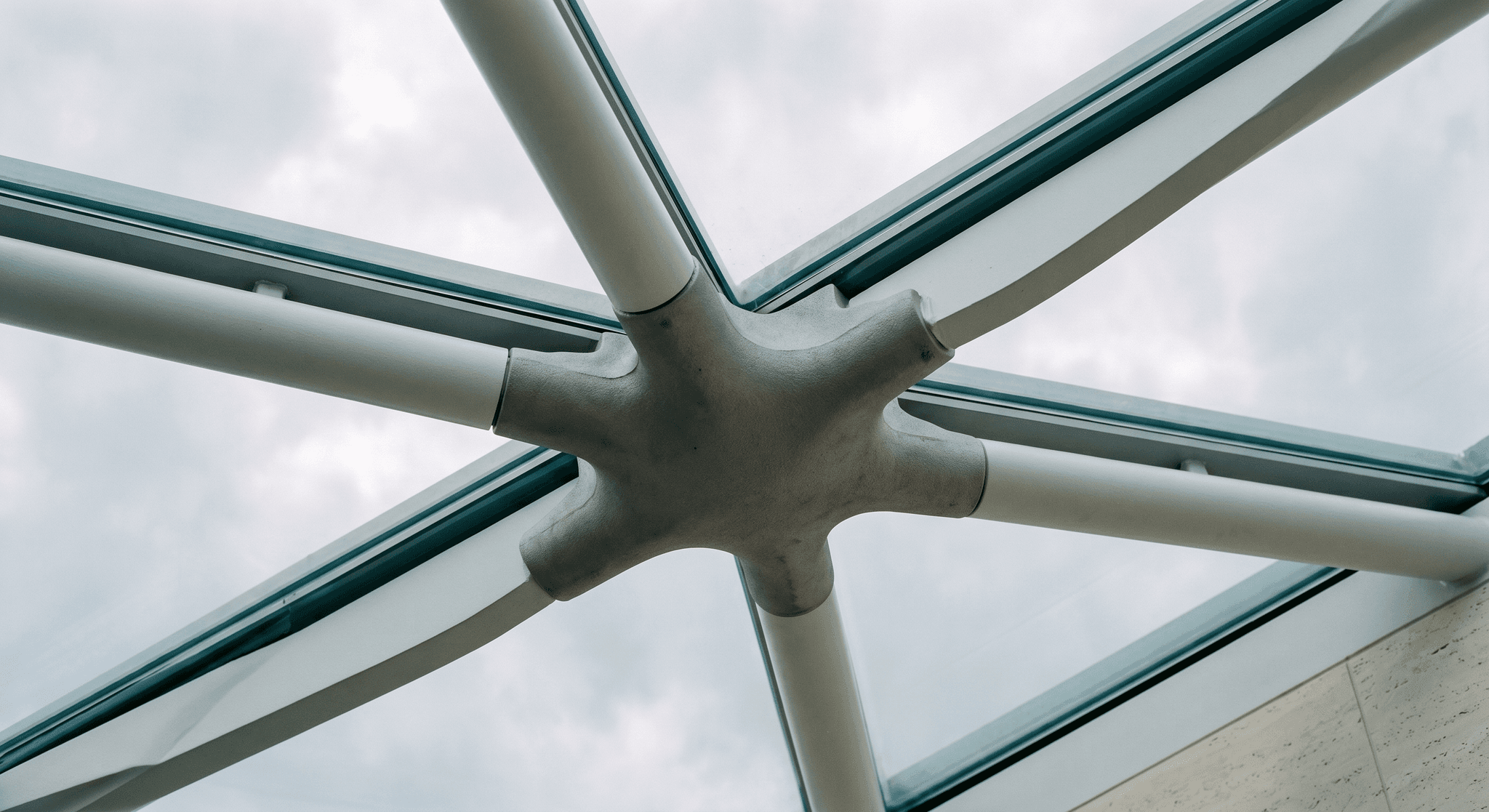 Detail of cast steel structural node, six chords converging at variable angles, sand-cast micro-texture, viewed from the atrium